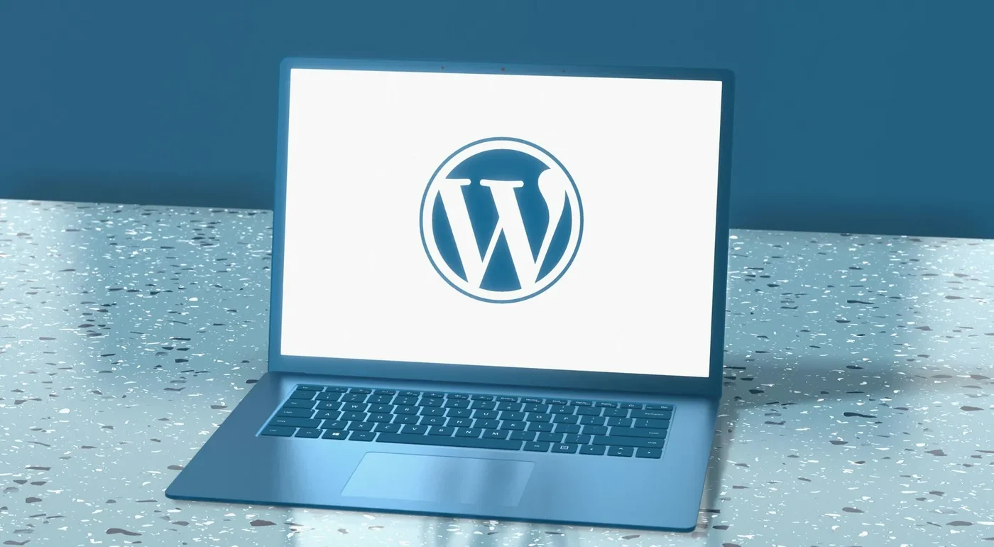 A laptop showing the WordPress logo on a blue speckled desk.