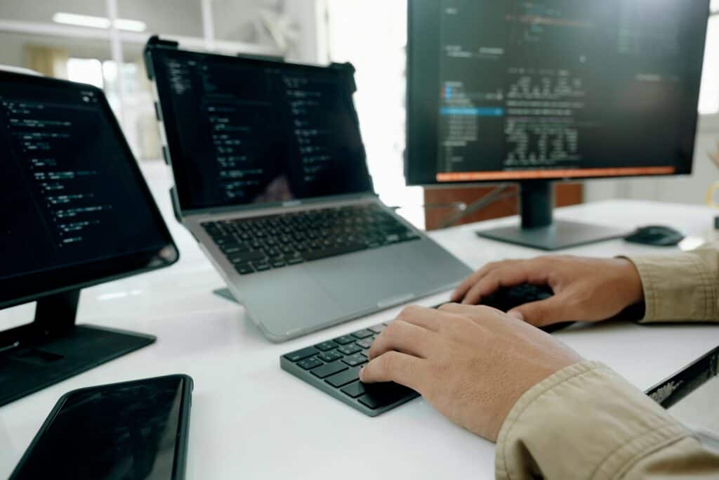 Hands typing at a keyboard with code on the monitors